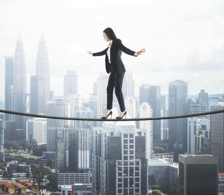 Photo of Woman, dressed in business attire, walking on a high wire, above a city scape